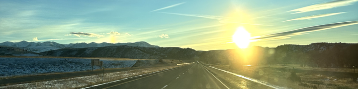 The interstate stretches ahead, with the sun setting, clouds streaking across the sky.